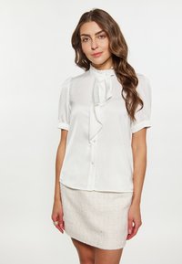 Blusa bianca a maniche corte con un colletto a ruffles e allacciatura con bottoni, realizzata in tessuto liscio, abbinata a una gonna chiara di tessuto testurizzato.