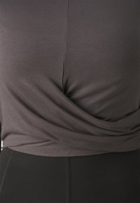 Gray, fitted top made of soft fabric with a twisted front design, paired with black high-waisted leggings featuring visible seams.