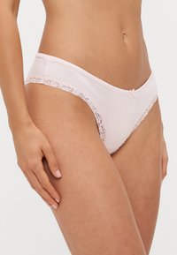 Light pink cotton panties with lace trim along the waistband and legs, featuring a small bow accent at the center front.