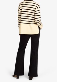 Pull en tricot ivoire avec des rayures noires, présentant une coupe décontractée et une texture côtelée. Associé à un pantalon en velours côtelé noir évasé et des chaussures à talons.