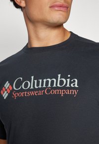 Černé bavlněné tričko s logem "Columbia Sportswear Company" v světle zelené a oranžové barvě, s kulatým výstřihem a krátkým rukávem.