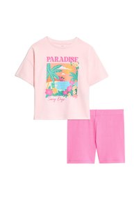 T-shirt in cotone rosa chiaro con grafica "PARADISE", che presenta foglie e fiori tropicali. Pantaloni corti in cotone rosa coordinati con una texture a coste.