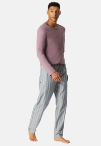 Maglietta viola a maniche lunghe con scollo a V abbinata a pantaloni da pigiama blu a righe con strisce arancione chiaro e bianco. Nessuna ferramenta visibile.