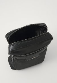 Sac noir en matériau texturé avec une fermeture éclair, présentant une accent en cuir à l'avant et un intérieur spacieux.