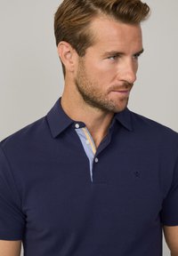 Polo shirt blu navy a maniche corte, con una patta a righe blu e giallo. Include un piccolo logo ricamato sul petto.