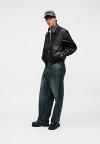 Μαύρο δερμάτινο μπουφάν τύπου bomber με φερμουάρ, συνδυασμένο με άνετο μπλε τζιν παντελόνι. Το μοντέλο φοράει γκρι καπέλο και χοντρές μαύρες πλατφόρμα παπούτσια.