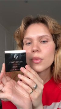 Evolutiion Powder i en firkantet svart etui med hvit tekst. Modellen holder den og viser fram sine glansfulle lepper og teksturerte hår.