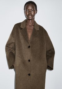 Brun uld oversized frakke med notched krave, to forlommer og tre sorte knapper. Blødt, tekstureret stof med en løs pasform.