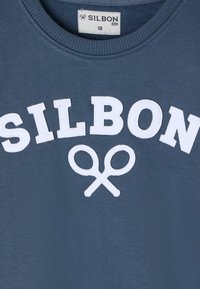 Sudadera azul con el texto "SILBON" en blanco y un gráfico de tijeras. Cuello redondeado y puños acanalados. Tela suave con una textura lisa. Talla 10.