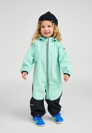 Mint green waterproof jacket with a zip front, black accents, and cuffs; paired with black pants and blue shoes. Curly hair and black beanie.