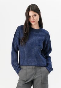 Maglione a coste blu scuro con colletto rotondo, spalle scese e vestibilità ampia. Abbinato a pantaloni cargo grigi, con tasche frontali.
