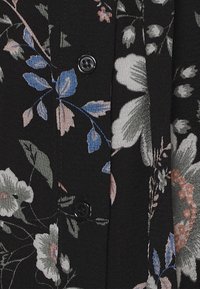 Tissu à motif floral noir avec des fleurs bleu clair et roses, comportant des boutons noirs visibles le long de la couture. Détails de surface texturés évidents.