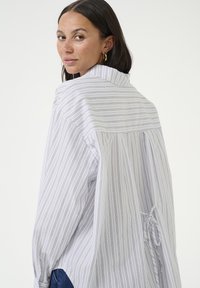 Striped button-up shirt in lightweight fabric. Features a collar, loose fit, and gathered detailing at the back. Colors include white, blue, and gray.