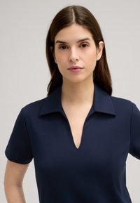 Donkerblauwe polo met korte mouwen, een kraag en een V-hals ontwerp. Gemaakt van een gladde stof met een aansluitende pasvorm.