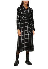 Schwarzes Karokleid mit grauen Linien, langen Ärmeln, Knopfleiste, Taillengürtel und knielangem Saum. Getragen mit schwarzen Stiefeletten.