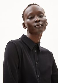 Schwarzes Hemd mit Kragen, mit einem durchgehenden Knopfverschluss, weicher Textur und sichtbaren Nähten. Sauberes, minimalistisches Design.