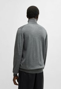 Grauer Pullover mit hohem Hals, aus strukturiertem Stoff. Hat lange Ärmel, gerippte Bündchen und einen geraden Saum.