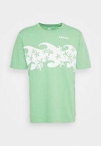 T-shirt Levi's vert clair avec un design de vagues et de fleurs blanches sur la poitrine et des manches courtes.