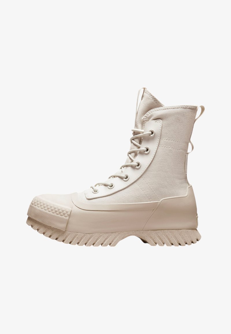 White high-top boots featuring a canvas upper, rubber toe cap, textured sole, and metal eyelets with laces. Side loops for easy wear.