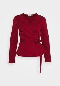 Haut cache-cœur rouge à manches longues, col en V et ceinture en tissu. Texture lisse avec une taille peplum. Design simple sans motifs supplémentaires.