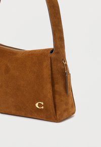 Hnědá semišová kabelka s horním zipem, krátkým popruhem a malým zlatým kovovým logem "C" v dolním rohu.