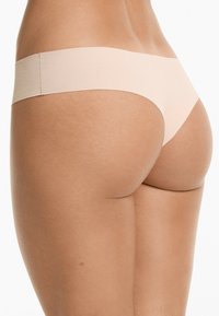 Nude naadloze string met een zachte, gladde textuur en een minimale elastische tailleband, voorzien van een klassieke snit en laag uitgesneden ontwerp.