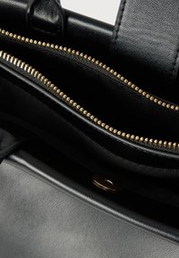 Črna usnjena torba z zlatim zadrgo, delno odprta, prikazuje prazen notranjost in teksturiran usnjen zunanji del.