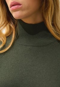 Donkergroene coltrui met een fijne geribbelde textuur, ronde hals en een slimfit ontwerp. Zichtbare stikseldetails en een gladde stofafwerking.