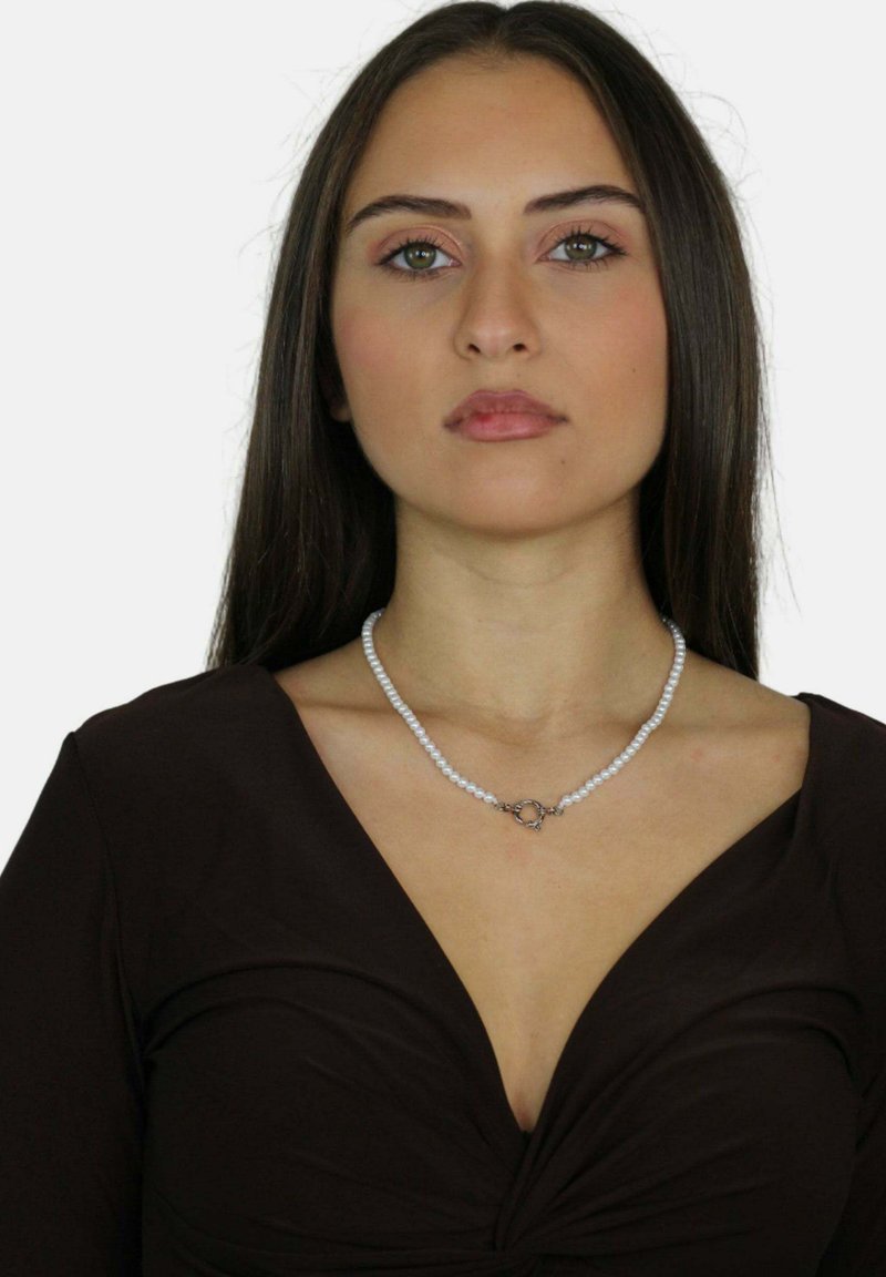 Collana di perle con chiusura in argento, caratterizzata da perle bianche rotonde, indossata da una modella con un top marrone a maniche lunghe e scollo a V profondo.