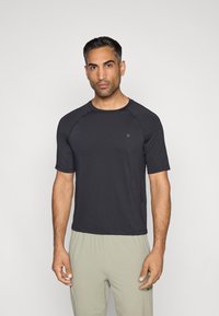 Īsām piedurknēm sporta krekls tumšā pelēkā audumā, ar raglanu piedurknēm un mazu logo uz krūšu daļas, gluda tekstūra un brīva piegriezuma fasonā.