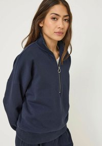 Felpa blu navy con collo alto, chiusura con mezza zip e tessuto testurizzato. Presenta spalle cadute e vestibilità rilassata.