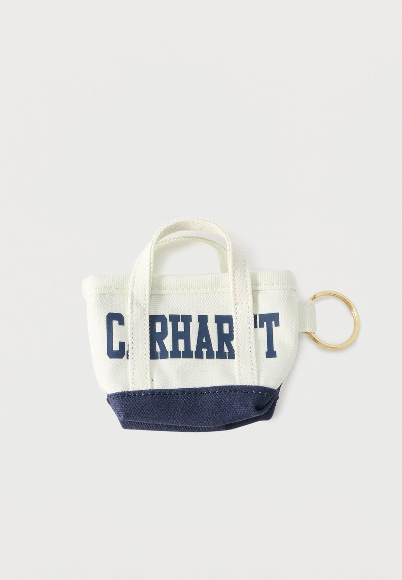 Portachiavi a forma di borsa in tessuto bianco e blu navy con due manici, la scritta "CARHARTT" stampata in blu navy e un anello portachiavi in metallo dorato sul lato.