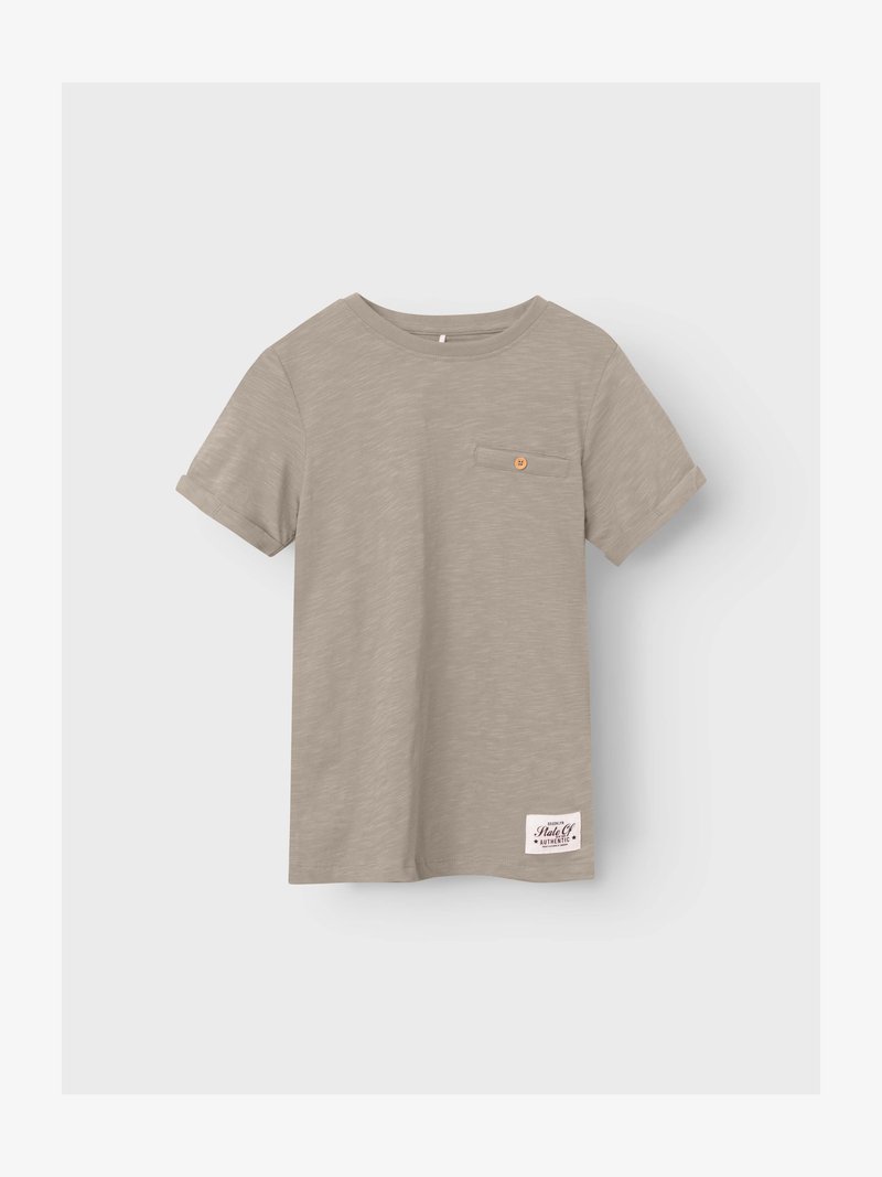 Μπεζ κοντομάνικη μπλούζα με μικρό τσεπάκι στο στήθος με κουμπιά και ένα λευκό ορθογώνιο ετικέτα κοντά στο κάτω τελείωμα.