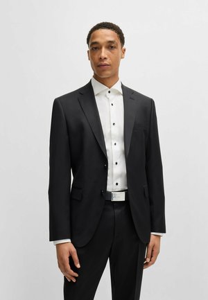 Costume noir ajusté avec une veste à un bouton, une chemise blanche avec des boutons noirs et une ceinture à accents argentés. Texture de tissu lisse.