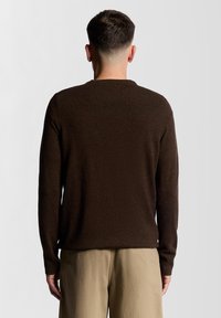 Καφέ πλεκτό πουλόβερ με μακριά μανίκια, λαιμόκοψη με στρογγυλή λαιμόκοψη και υφή, συνδυασμένο με ανοιχτό μπεζ παντελόνι. Εμφανίζεται η πίσω όψη.