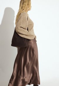 Beiger Pullover mit entspannter Passform und gerippter Textur, kombiniert mit einem fließenden dunkelbraunen Satinrock und einer dunkelbraunen Einkaufstasche.