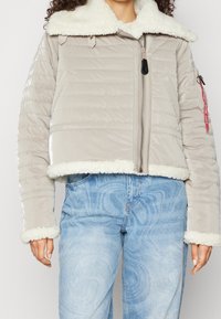 Lekko ocieplana, szara krótka kurtka z miękkim, białym kołnierzem i mankietami z imitacji futra; posiada boczne kieszenie i zapinana jest na zamek z przodu.