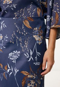 Stof met bloemmotief in marineblauw, met witte en koperen accenten. Glad textuur met opvallende bloem- en bladontwerpen.