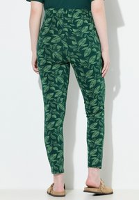 Leggings verts avec un motif de feuilles en vert clair, fabriqués dans un matériau lisse, à coupe ajustée, avec une taille haute et une longueur jusqu'aux chevilles.