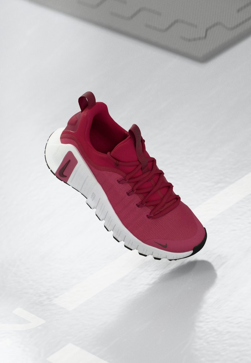 Scarpa sportiva rossa con tomaia texturizzata, lacci e suola spessa bianca. Presenta un cappuccio nero contrastante e un logo sul lato.