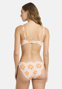 Twee-delig bikini met een geruit patroon in wit en oranje, versierd met bloemenaccenten. De top heeft verstelbare banden en een haaksluiting.
