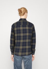 Camisa a cuadros en tonos marino y oliva, con mangas largas, puños abotonados, collar y dobladillo recto. Textura suave y diseño estructurado.