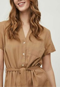 Robe marron boutonnée, manches courtes, col et ceinture à la taille. Comprend une poche avant et un tissu doux et texturé.