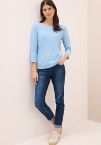 Maglione a maniche lunghe azzurro chiaro abbinato a jeans blu scuro e sneakers beige con dettagli azzurri chiari. Outfit semplice e casual.