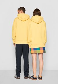 Gule hetter, oversized passform, bomullsblanding; paret med marineblå joggebukser og et flerfarget rutete skjørt. Uformelle sko i mørke toner.