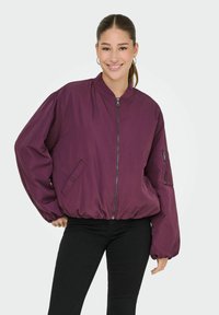 Violet bomber stiliaus striukė su užtrauktuku priekyje, elastinga juosmens linija ir šoninėmis kišenėmis. Puikus minkštas audinys ir apimties pilni rankoviai.