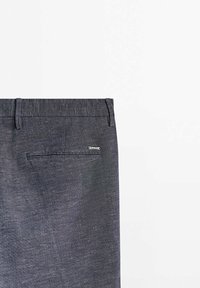 Pantalon en tissu texturé gris foncé montrant la taille arrière avec des passants pour ceinture et une poche arrière passepoilée unique avec une petite étiquette métallique de marque.