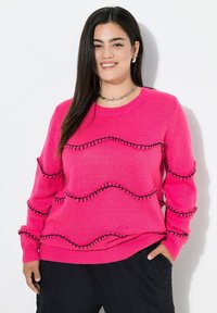 Suéter de punto rosa brillante con acentos de costura en negro en forma de ondas. Cuello redondo, mangas largas y puños y dobladillo acanalados. Tejido texturizado.