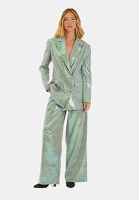 Completo a quadri iridescenti composto da un blazer doppiopetto e pantaloni a gamba larga. Il materiale riflette la luce, mostrando una lucentezza metallica.