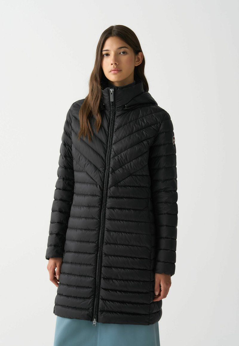 Melna pūkainā jaka ar ševronu rakstu, ar kapuci un priekšējo rāvējslēdzēju. Iezīmējas ar quilted sekcijām un gludu, spīdīgu tekstūru.